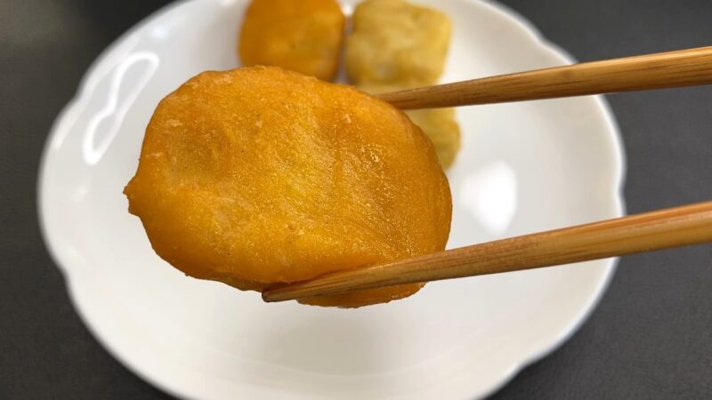 箸で持ち上げた国産チキンナゲットのアップ。衣はこんがりとしたきつね色で、表面はツヤがありサクッとした質感。