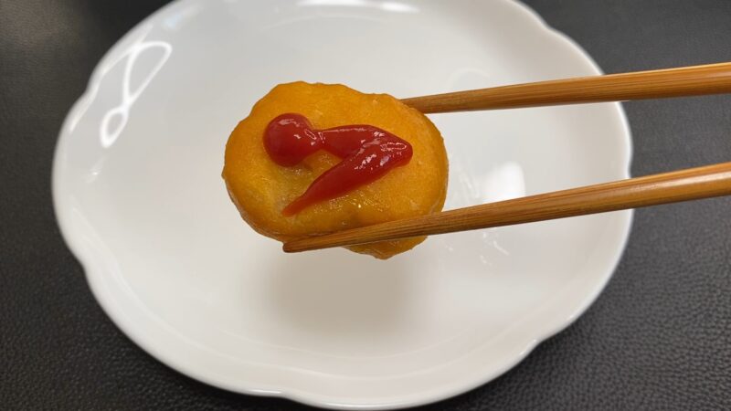 ケチャップをのせた国産チキンナゲット。赤いソースが映えて、箸で持ち上げている。