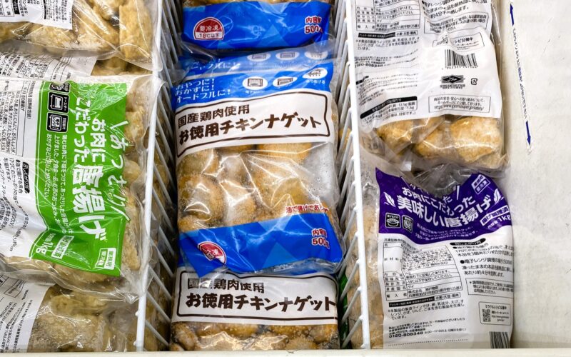 業務スーパーの冷凍食品コーナーに並ぶ「お徳用チキンナゲット(国産)」。青いパッケージが目印で、隣には唐揚げや他の冷凍惣菜も並んでいる。