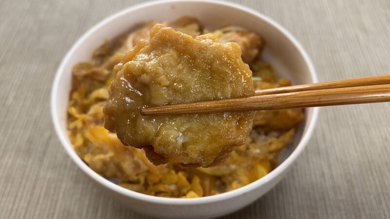 箸で持ち上げたチキンナゲット親子丼のナゲット。つゆと卵が絡んでつやつやしている。