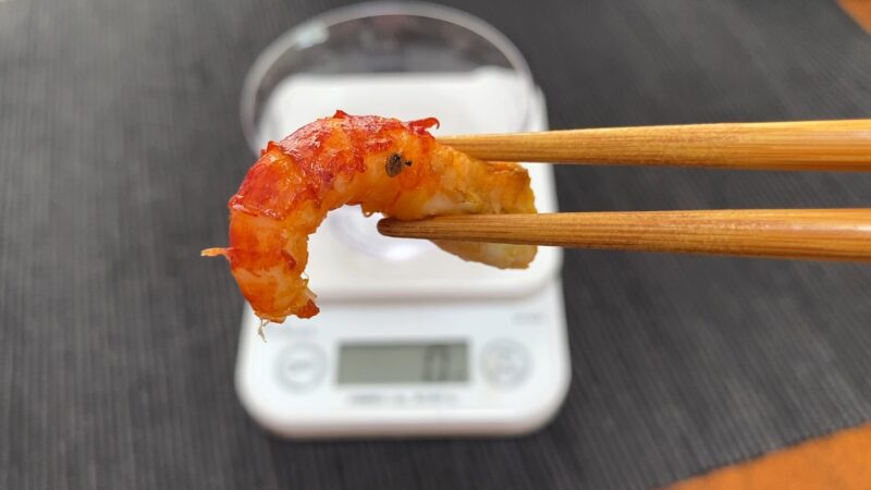 箸でつまんだザリガニの身。赤い殻と白身のコントラストが際立っている。