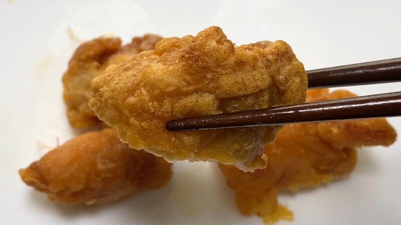 業務スーパー「和風鶏もも唐揚げ」をノンフライヤーで加熱後、箸で持ち上げた写真。衣はカリッとした質感で、香ばしく仕上がっている様子が伝わる。