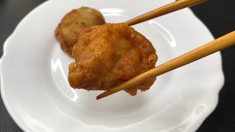 業務スーパー「和風鶏もも唐揚げ」を油で揚げたあと、箸で持ち上げた写真。衣はこんがりと色づき、揚げたてのツヤと香ばしさが感じられる。