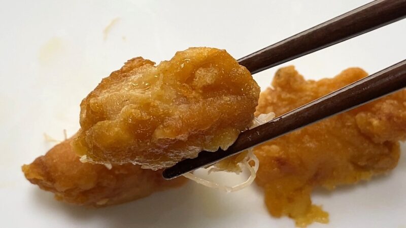 業務スーパー「和風鶏もも唐揚げ」を電子レンジで加熱後、箸で持ち上げた写真。衣がしっとりしており、全体的にやわらかい印象の仕上がり。