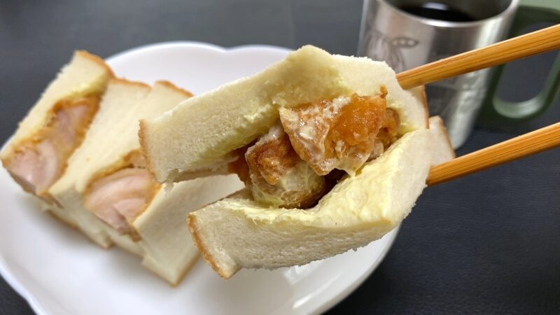 唐揚げサンドを箸で持ち上げて食べる直前のシーン。中には唐揚げとマヨネーズがぎっしり詰まり、朝食や軽食にぴったりの構成。