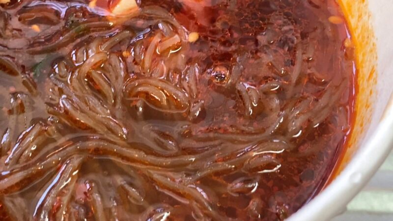 酸辣粉（サンラーフン）のスープをアップで撮影。唐辛子オイルが表面に浮かび、春雨にしっかりと辛味の赤色が絡んでいます。