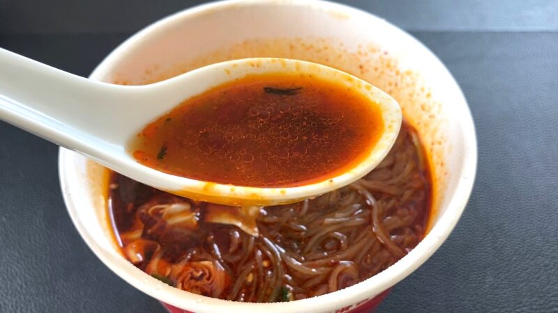 レンゲですくった酸辣粉（サンラーフン）のスープ。オレンジがかった赤色の油膜が浮かび、酸味と辛味が際立つ見た目です。