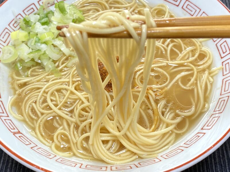 一蘭ラーメンの麺を箸で持ち上げた写真。ストレート麺の細さとスープの絡みがよく分かる。刻みネギのトッピング付き。