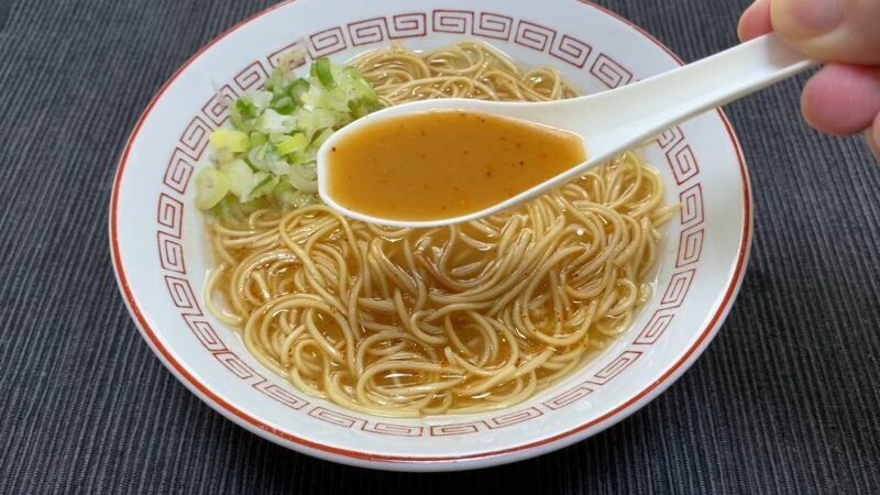 一蘭ラーメンのスープをレンゲですくった写真。中央に秘伝の赤い粉が溶け込み、スープがやや赤みを帯びている。辛味が加わった状態。