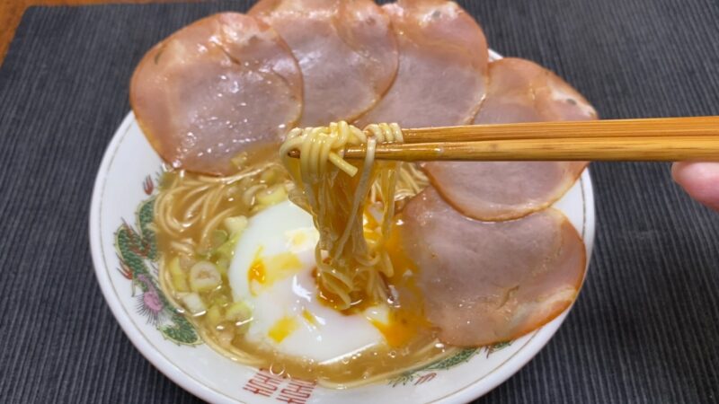 温泉卵を絡めた一蘭ラーメンを箸で持ち上げている写真。とろっとした黄身とスープが一体化して美味しそう。