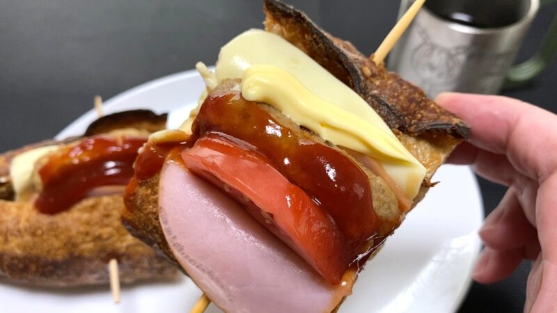 マヨネーズとケチャップをのせたミニハンバーグバゲットのアップ。トマトとハムを挟んだ断面がよく見える