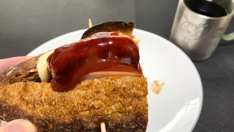 激辛ソースをたっぷりかけたミニハンバーグバゲット。ソースの艶と香ばしいパンの焼き目が際立つ