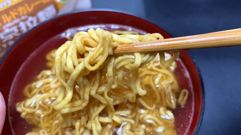 東京拉麺マイルドカレー味を箸で持ち上げた様子。麺にカレースープがしっかり染みているアップ写真。