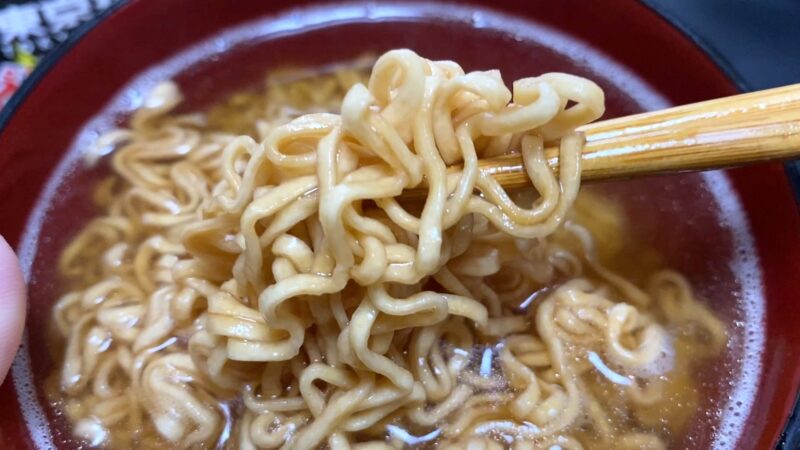 東京拉麺ピリ辛にんにく味の麺を箸で持ち上げたアップ写真。スープがよく絡み、にんにくの風味が際立つ。