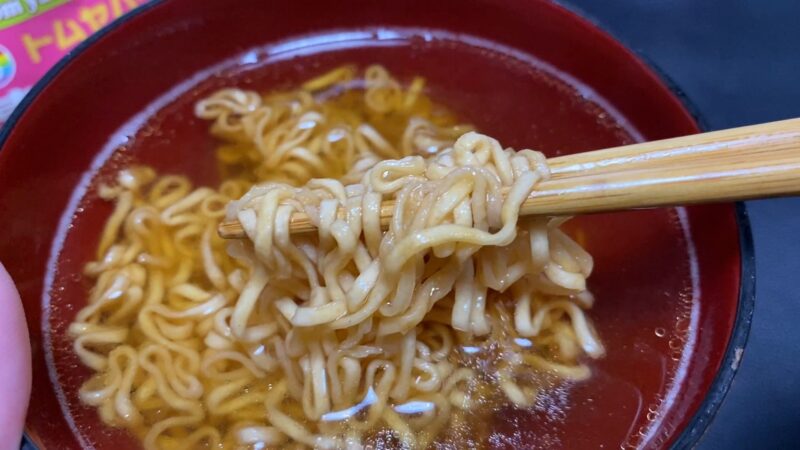 東京拉麺トムヤンクン味の麺を箸で持ち上げたアップ写真。スープがよく絡み、麺にツヤがある。