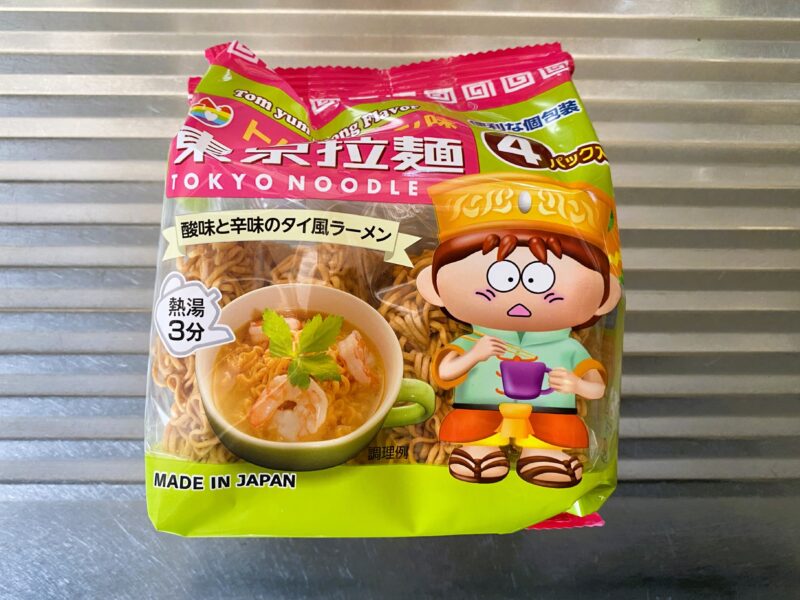 東京拉麺トムヤンクン味のパッケージ。ピンクと黄緑の袋に、タイ風の帽子をかぶったキャラクターが描かれている。