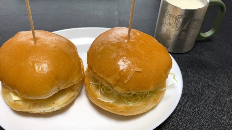 2つ並べた自家製トンカツバーガーを皿に盛り付けた写真。ふっくらしたバンズの中にキャベツととんかつが入り、朝食にも昼食にも合うボリューム感。