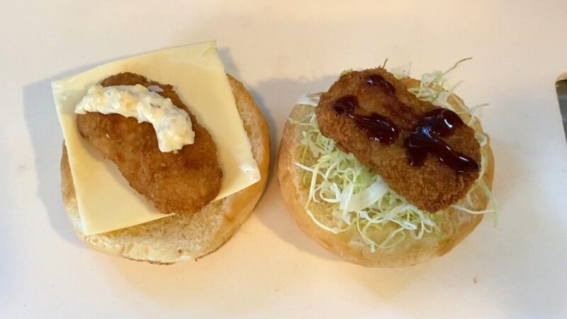 ハンバーガー用のバンズにキャベツとチーズを敷き、業務スーパーの冷凍とんかつをのせた状態。片方はソース、もう片方はタルタルソースで味付けしている。