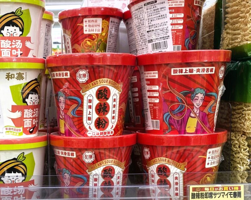 業務スーパーの店頭に並ぶ酸辣粉（サンラーフン）のカップ麺。赤いパッケージが目を引き、隣には白い酸湯面叶も陳列されています。
