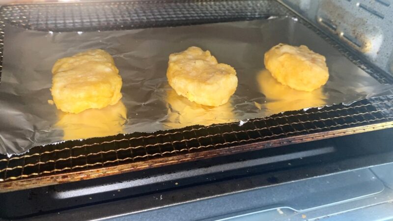 アルミホイルを敷いたトレーにチキンナゲットを並べ、オーブントースターで加熱している様子。表面がこんがり焼け始めている。