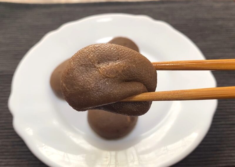 箸でつまんだ業務スーパー「ホイップクリーム大福(チョコ)」。 柔らかく伸びるお餅の質感が印象的で、もっちり感が伝わる。