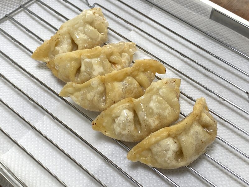 揚げた豚肉餃子が5個、キッチンペーパーを敷いた網に並んでおり、皮がふくらんで薄く色づいている。