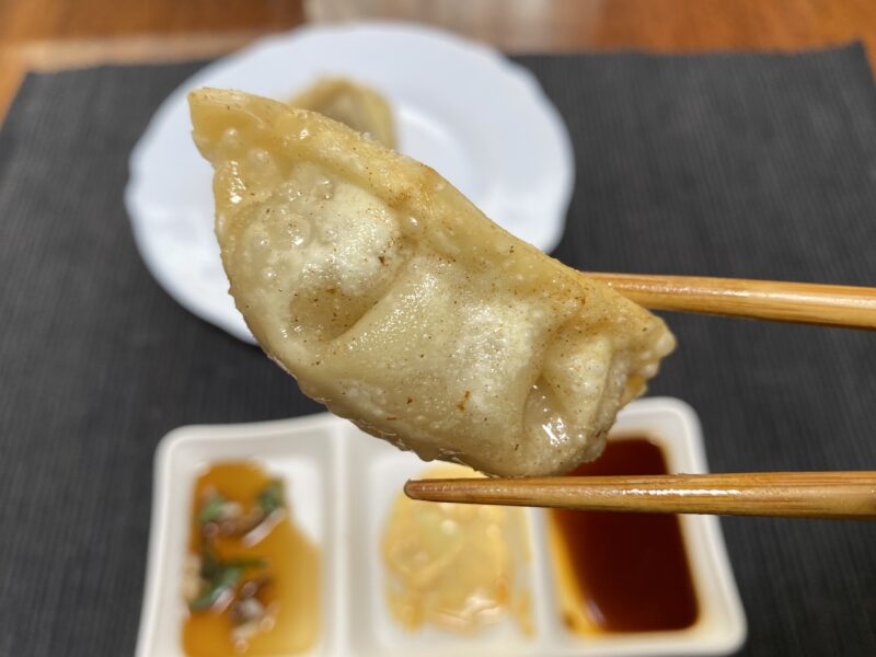箸で持ち上げた揚げ餃子のアップ写真で、皮がふっくらし、表面に細かい気泡と軽い色づきが見える。