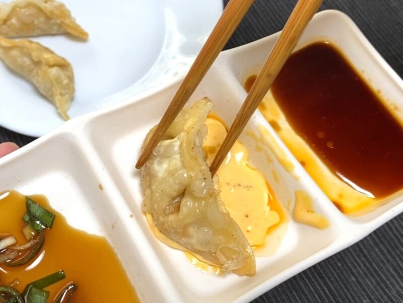 揚げ餃子を箸で持ち、マヨネーズとラー油を合わせたタレに浸している様子を写した写真。隣には醤油系のタレも見える。