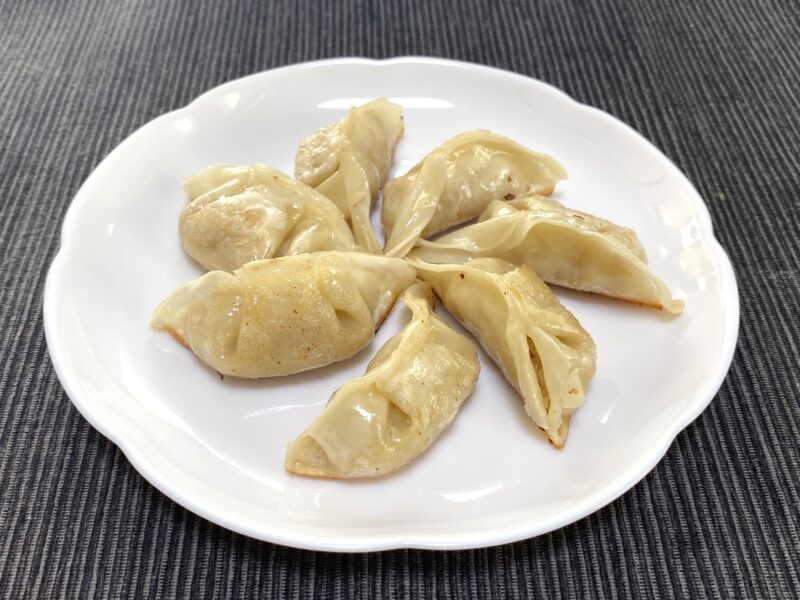 白い皿に焼き上げた豚肉餃子が7個並んでおり、皮はつやがあり、底面に軽い焼き色がついている。