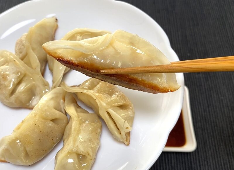箸で持ち上げた焼き餃子の底面に、きつね色の焼き目がついている様子が分かるアップ写真。