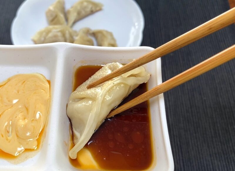 焼き餃子を箸で持ち、醤油とラー油のタレに浸している様子を写した写真。左の区画にはマヨ＋ラー油のソースが入っている。