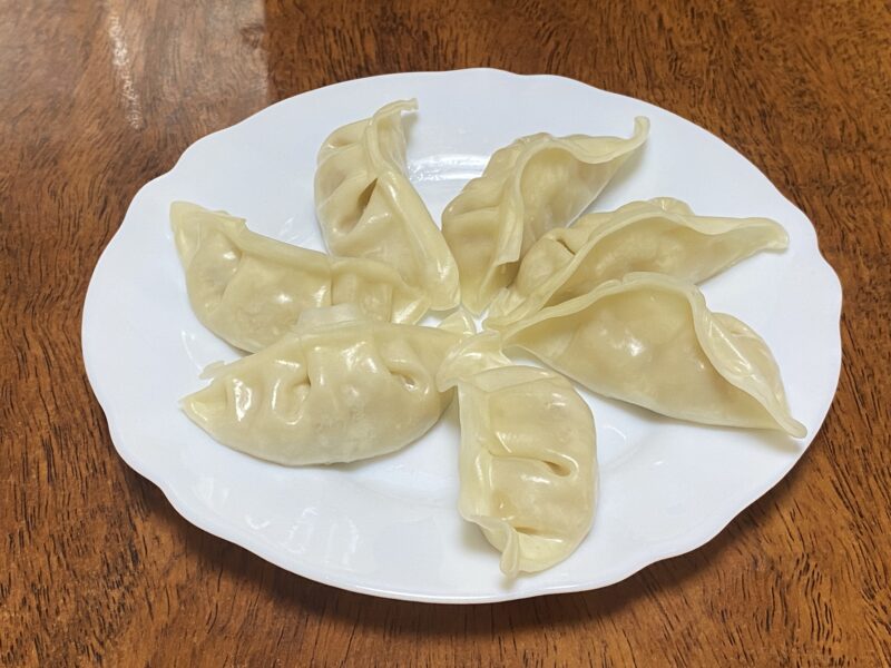 白い皿に蒸した豚肉餃子が7個並んでおり、皮がぷるっとふくらんでつやがある状態。