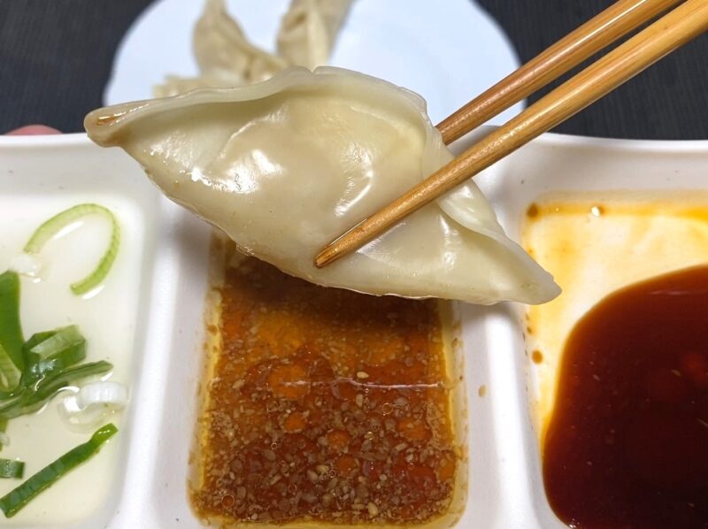 蒸した餃子を箸で持ち、香味しょうゆダレ（ラー油と刻み具材入り）の部分に浸している様子を写した写真。隣には別のタレも見える。