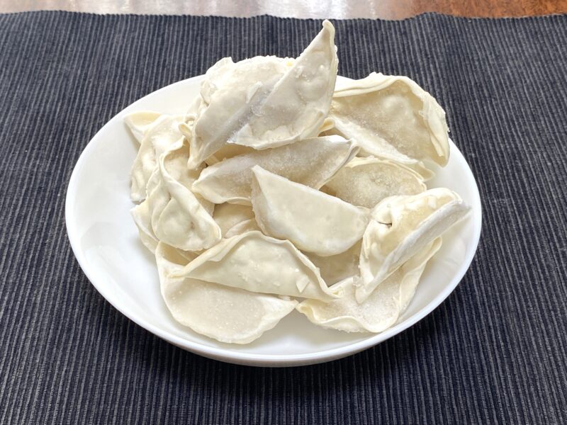 業務スーパーの豚肉餃子を凍ったまま白い皿に盛り付けた写真。全体の大きさや形が分かる。
