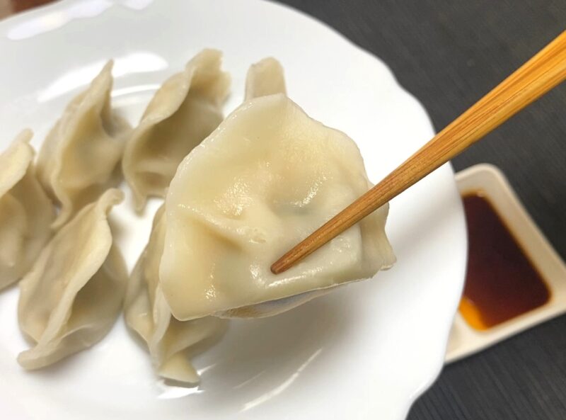 箸で持ち上げた茹でた三鮮水餃子のアップ。厚めの皮がつるっと光り、弾力のある質感が伝わる。