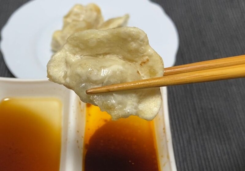 箸で持ち上げた揚げ三鮮水餃子のアップ。表面の気泡が揚げたてらしい軽いサクサク感を伝える。