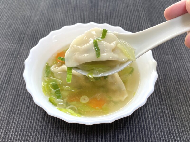 スープに浸った三鮮水餃子をレンゲで持ち上げたアップ。皮がスープを吸ってふっくらしており、野菜も一緒に写っている。