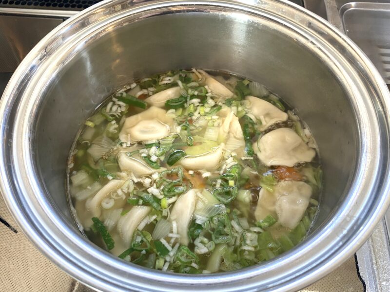 鍋の中で三鮮水餃子と野菜を煮込んでいる様子。ネギ、キャベツ、にんじんと一緒にスープで加熱されている。