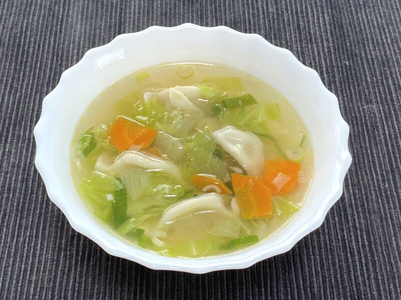 三鮮水餃子を具だくさんの野菜スープに入れ、白い器に盛り付けた様子。やさしい色合いの澄んだスープ。