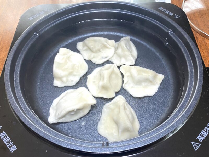 三鮮水餃子を茹で料理している。冷凍状態の餃子がお湯に沈んでいる