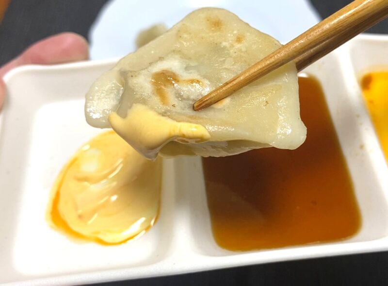 マヨネーズとラー油のタレにつけている焼き三鮮水餃子。焼き目が見える断面がアップで写っている。