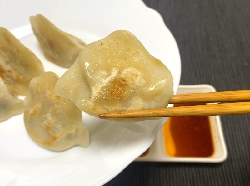 箸で持ち上げた焼き三鮮水餃子。底面に軽い焼き目がつき、皮のもちっとした質感が見える。