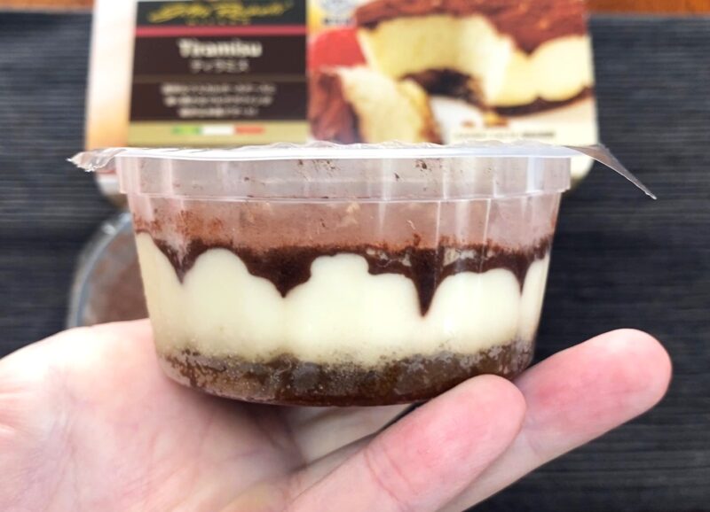 手に持ったカップ入りティラミスの横から見た層の状態。ココア、ムース、スポンジの3層がはっきり見える。