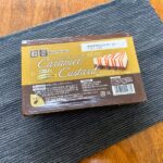 業務スーパーのカラメルカスタードのパッケージをテーブルの上に置いた様子。黄色と茶色のシンプルなパッケージが写っている。