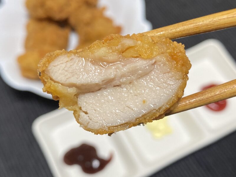 油調理した唐揚げの断面を箸で持ち上げた様子。中はしっとりとした鶏もも肉で、肉汁がにじんでいる。