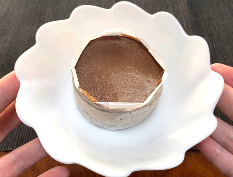 業務スーパー「ガトーショコラの誘惑」を白い皿に移した状態の画像。まだ冷凍状態で、常温1時間の解凍が必要な様子がわかる