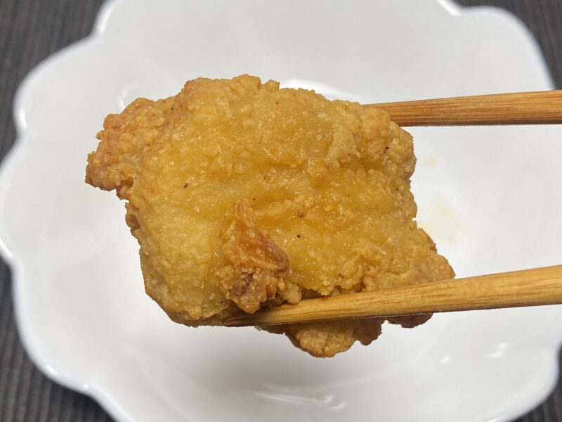 ノンフライヤーで調理した業務スーパー「お肉にこだわった美味しい唐揚げ（タイ産）」を箸で持った試食シーン。衣のザクザク感が分かるアップ。
