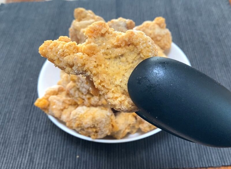 業務スーパー「お肉にこだわった美味しい唐揚げ（タイ産）」をトングでつまんだアップ写真。衣のザクザク感がわかるカット。
