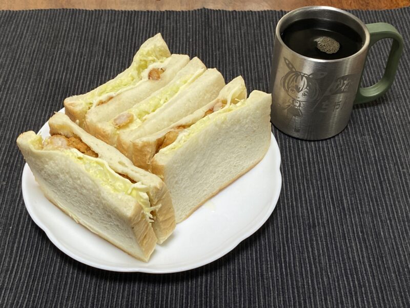 唐揚げサンドを食べやすくカットして皿に並べ、隣にホットコーヒーを置いた完成盛り付け写真。