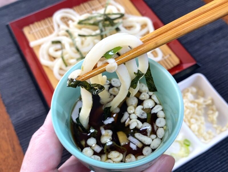 ネギと揚げ玉を乗せたざるうどん つゆにくぐらせた様子